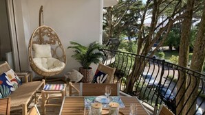 Un balcone con mobili in vimini, un tavolo da pranzo per due persone e vista sulla strada e sugli alberi.