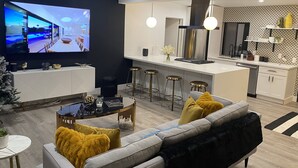 Ein modernes Wohnzimmer mit Fernseher, Essbereich und Küche mit Barhocker.