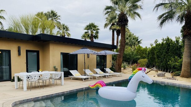Ein Schwimmbecken mit einem Einhorn-Schwimmspielzeug, Liegestühlen und einem Tisch mit Stühlen.