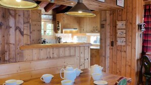 Un interior de madera con una mesa de comedor dispuesta para una comida, paredes de madera y una zona de cocina al fondo.