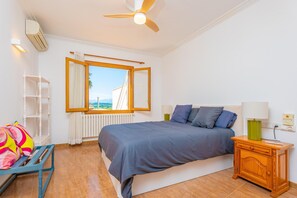 Ein Schlafzimmer mit Bett, Nachttisch, Fenster mit Vorhängen, Deckenventilator und Heizkörper.