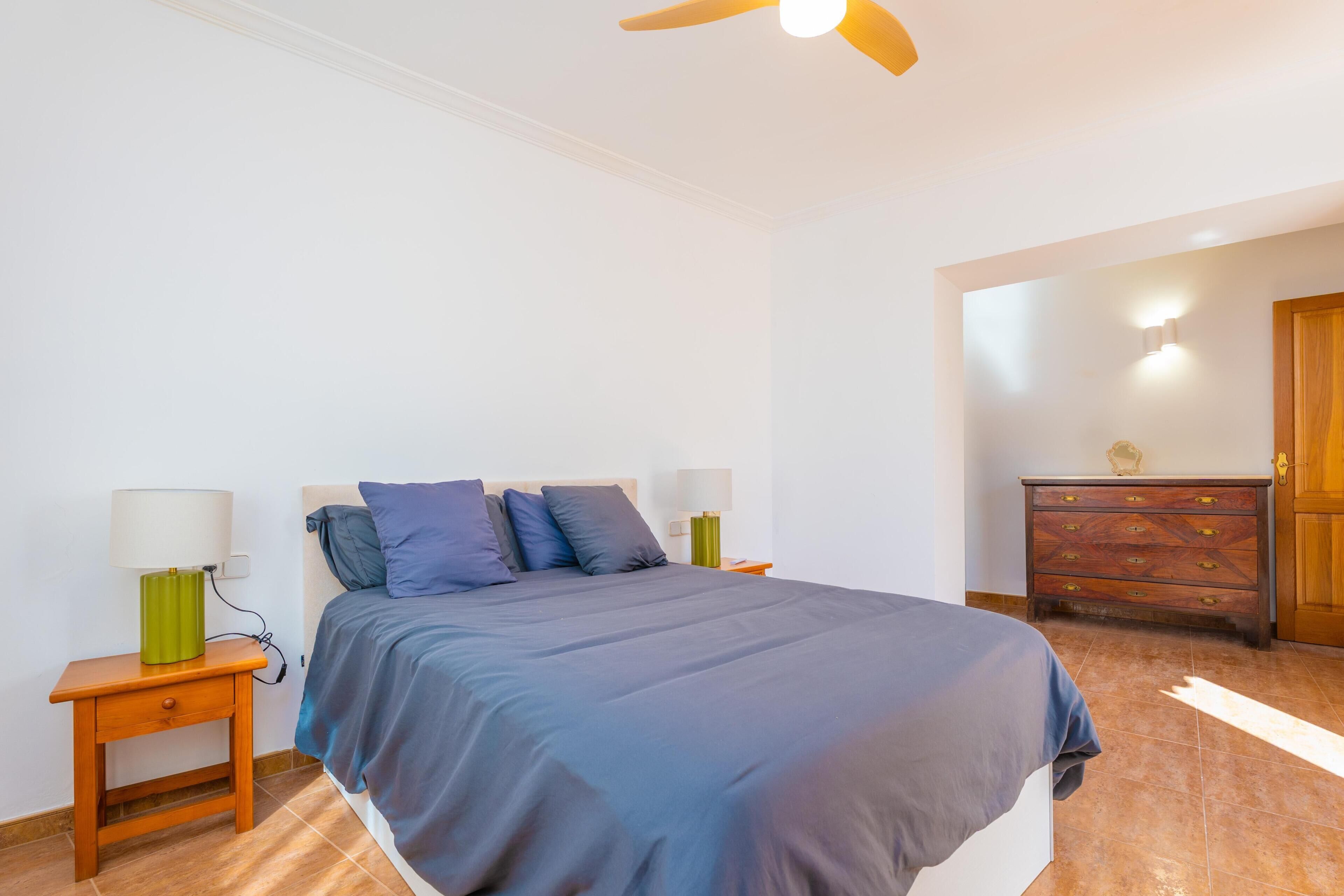 Une chambre à coucher avec un lit, deux tables de chevet avec des lampes, une commode et un ventilateur de plafond.