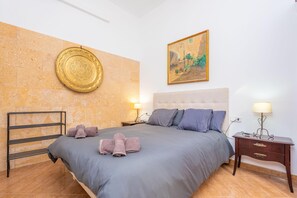 Une chambre à coucher comprenant un lit, une tête de lit, une table de chevet avec une lampe, un plateau fixé au mur et un tableau.