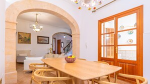 Et spiseområde med et træbord og stole, en lysekrone samt udsigt gennem en glasdør.