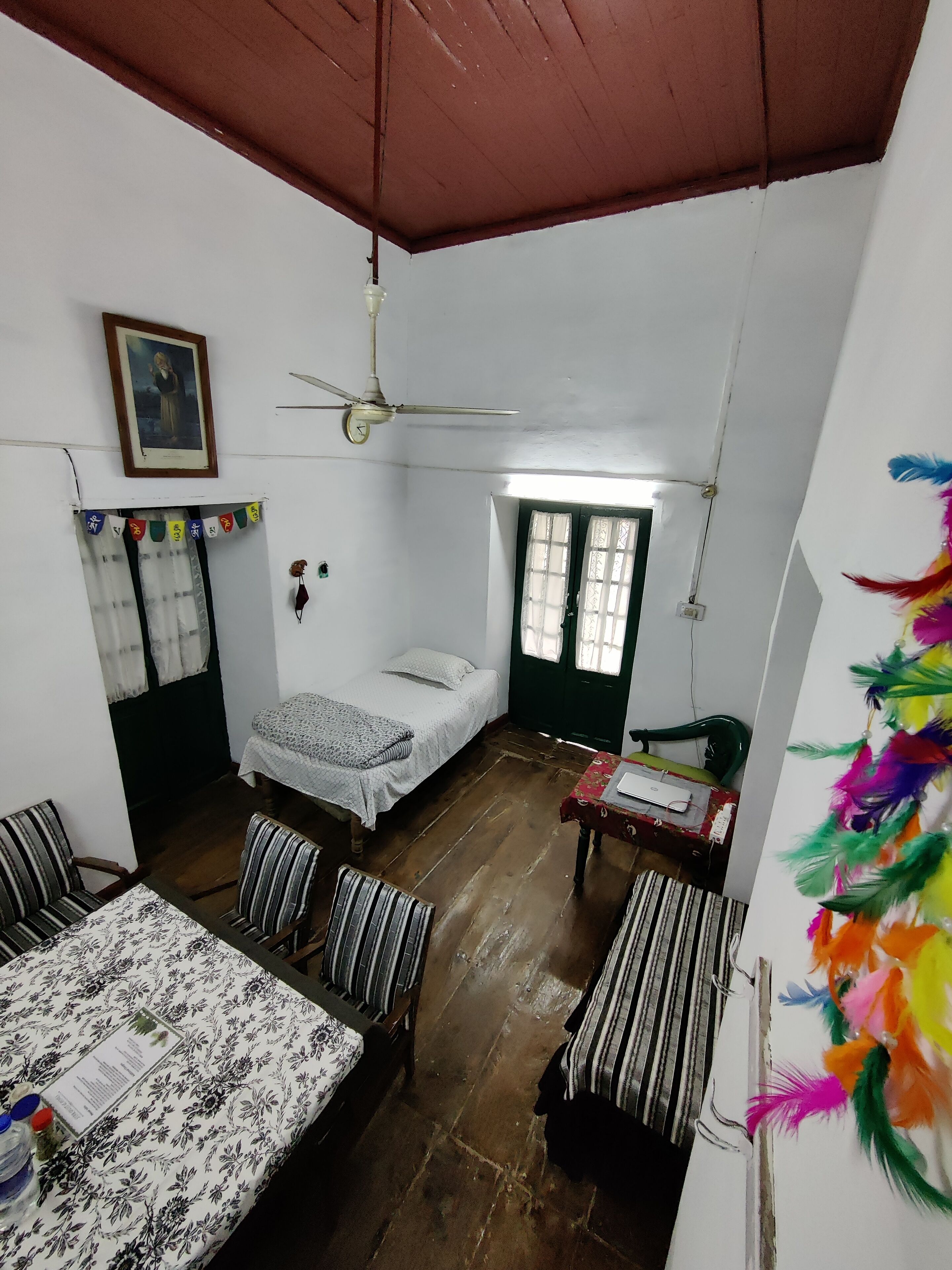 A room with a bed, a table, chairs, a ceiling fan, and a window.