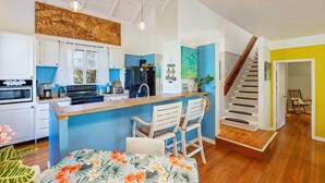 A modern kitchen with white cabinets, a blue accent wall, and a wooden island with bar stools. - Molokai Oceanfront large beautiful home - Gorgeous secluded beaches out front! (Maunaloa)