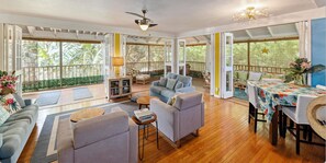 A spacious living area with a wooden floor, a sofa, a coffee table, and a dining table with a floral tablecloth.