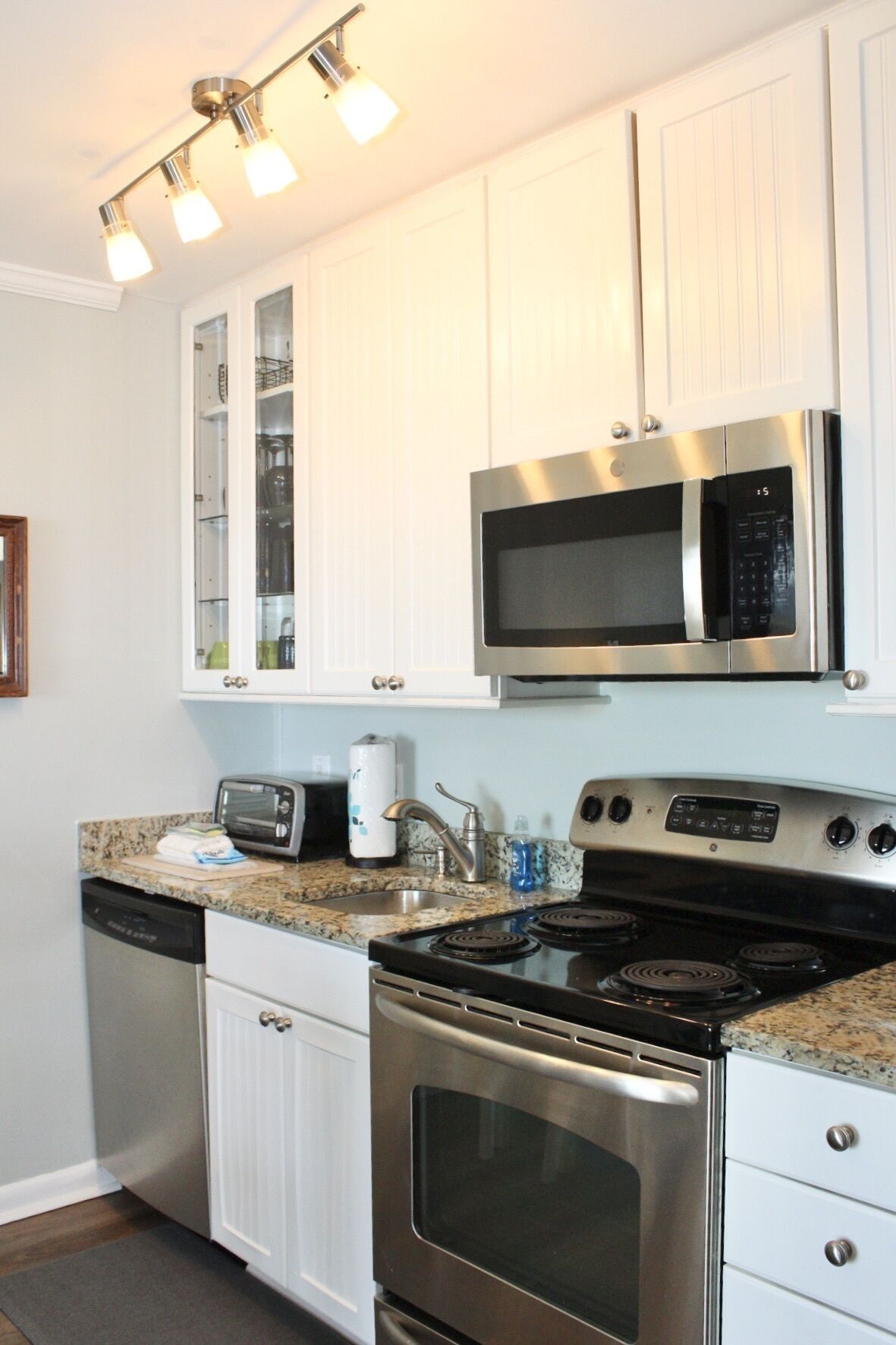A compact kitchen with white cabinets, a built-in microwave, a stove, and a toaster.