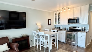 A modern kitchen with white cabinets, a built-in microwave, and an oven. There is a dining area with a table and chairs. - Modern Ocean Front Condo!! Community Pool & Pier! (Isle Of Palms)