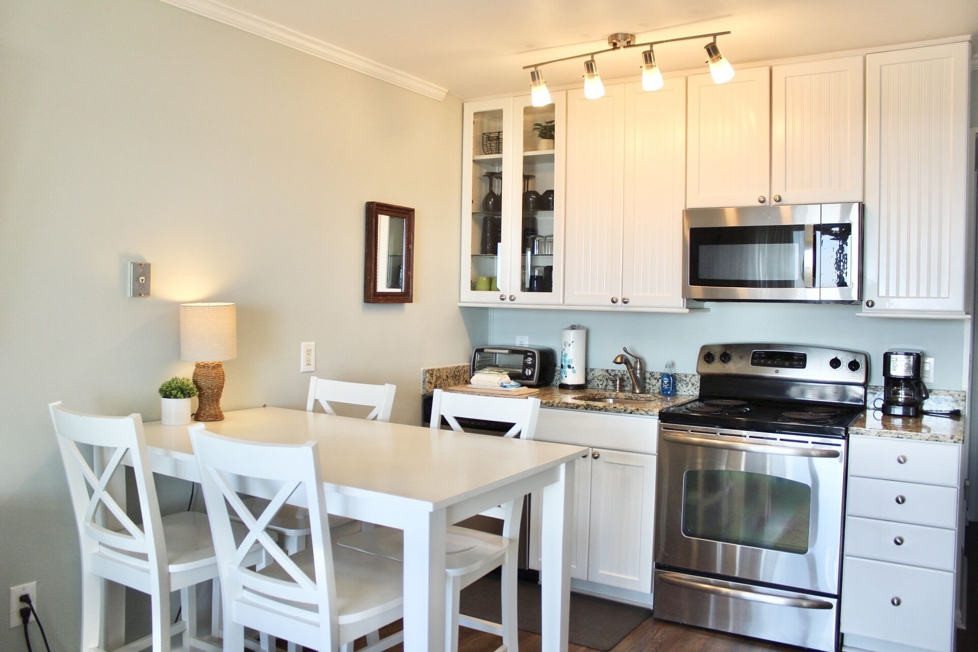 A modern kitchen with white cabinetry, stainless steel appliances, and a dining area with white chairs.