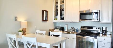 A modern kitchen with white cabinetry, stainless steel appliances, and a dining area with white chairs.