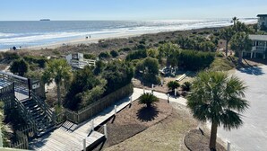 A beach view with a wooden boardwalk, palm trees, and a distant ship. - Modern Ocean Front Condo!! Community Pool & Pier! (Isle Of Palms)