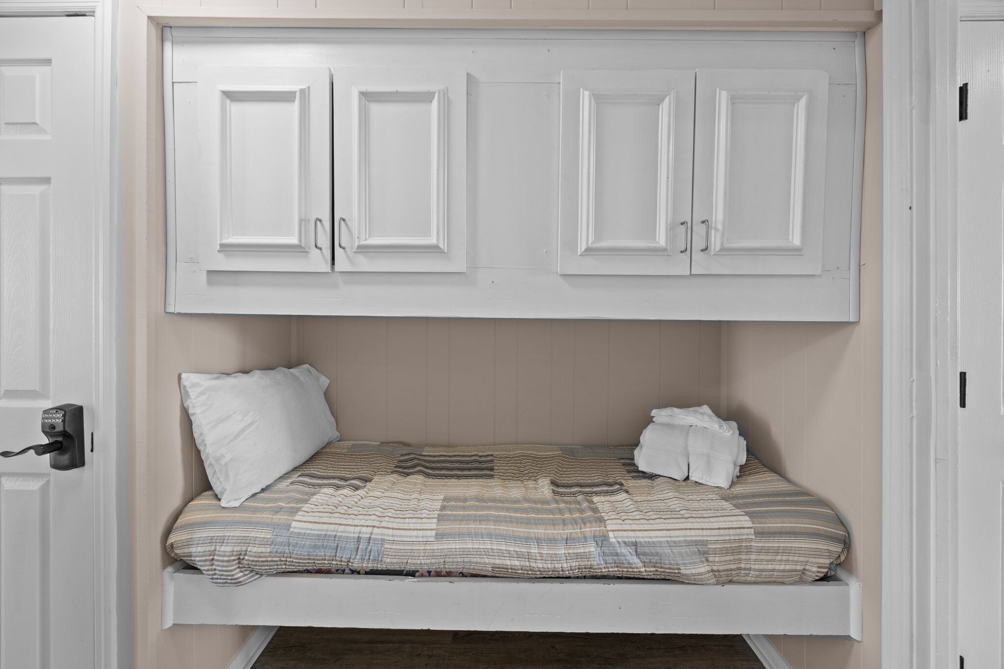 Een kleine kamer met een enkel bed en een inbouwkast boven het bed.