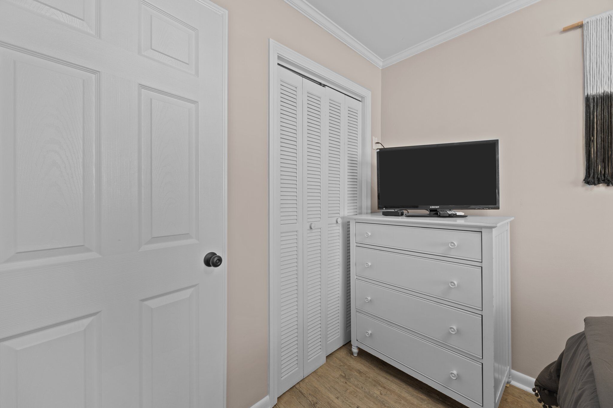 Een kamer met een witte deur, een witte dressoir met lades, een flatscreen televisie erboven en een kast met witte verstelbare deuren.