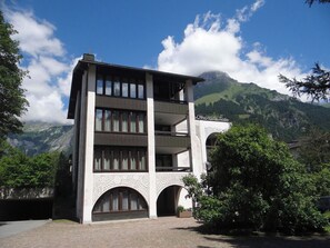 Un edificio de varios pisos con balcones, arcos y montañas al fondo.
