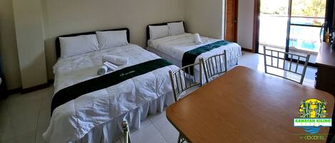 Habitación de hotel con dos camas, una mesa de comedor de madera y una puerta corrediza de vidrio que da a una zona de piscina.