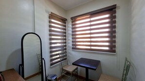 Une petite pièce bien éclairée, avec deux fenêtres, une chaise, une table et un miroir.