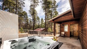 A hot tub in a wooded area with a wooden cabin in the background. - The Great Escape by Ruidoso Vacation Rentals (Ruidoso)