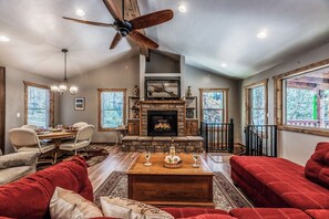 A living room with a fireplace, red sofas, a dining table with chairs, and a ceiling fan. - The Great Escape by Ruidoso Vacation Rentals (Ruidoso)