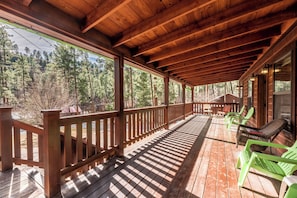 A wooden deck with a railing, green chairs, and a view of a forest. - The Great Escape by Ruidoso Vacation Rentals (Ruidoso)