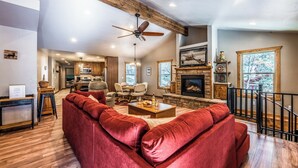 A spacious living room with a red sofa, wooden ceiling beams, a fireplace, and a kitchen in the background. - The Great Escape by Ruidoso Vacation Rentals (Ruidoso)