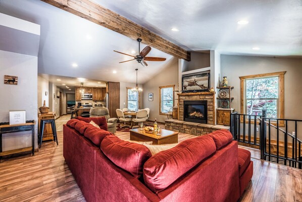 A spacious living room with a red sofa, wooden ceiling beams, a fireplace, and a dining area. - The Great Escape by Ruidoso Vacation Rentals (Ruidoso)