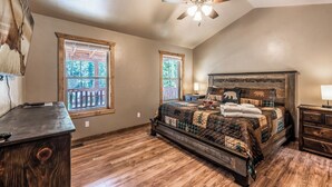 A bedroom with a large bed, wooden floor, two windows, a ceiling fan, and a nightstand. - The Great Escape by Ruidoso Vacation Rentals (Ruidoso)
