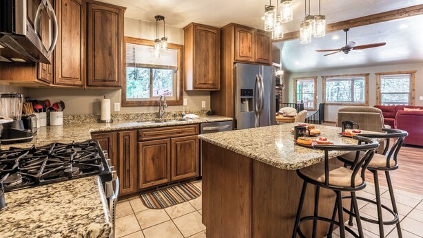 A spacious kitchen with granite countertops, wooden cabinets, a stainless steel refrigerator, and a bar area with stools. - The Great Escape by Ruidoso Vacation Rentals (Ruidoso)