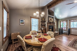 A dining area with a round table, chairs, and a chandelier. There are windows and a fireplace in the background. - The Great Escape by Ruidoso Vacation Rentals (Ruidoso)