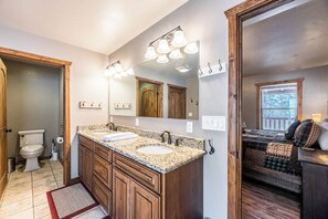 A bathroom with a double sink, wooden cabinets, a large mirror, and a red rug. - The Great Escape by Ruidoso Vacation Rentals (Ruidoso)