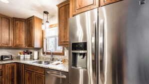 A kitchen with wooden cabinets, stainless steel appliances, a built-in dishwasher, and a window with blinds. - The Great Escape by Ruidoso Vacation Rentals (Ruidoso)