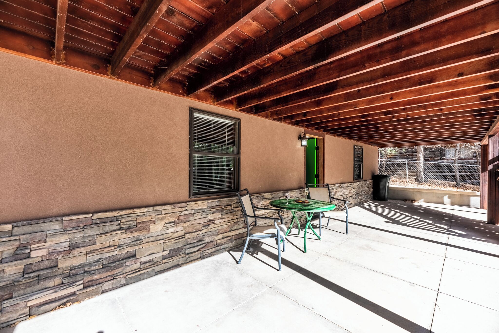 Un espace extérieur aménagé en terrasse, avec un mur en pierre, un plafond en bois et une table entourée de chaises.