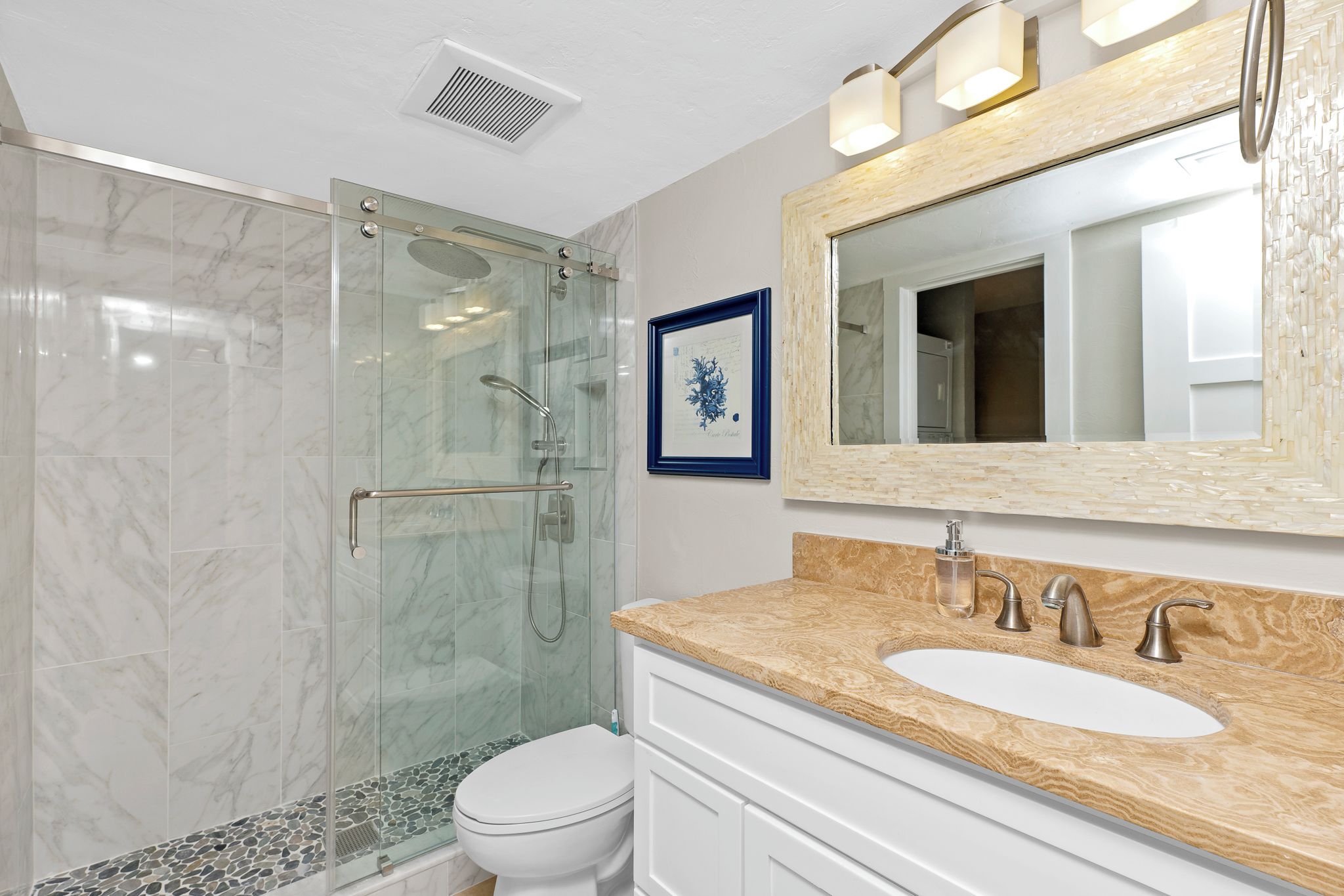 A modern bathroom with a glass shower enclosure, a white toilet, a vanity with a marble countertop, and a large mirror.