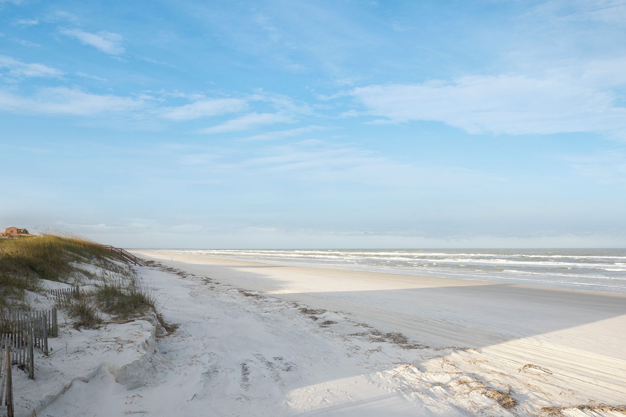 A beach with a wooden fence and dunes.