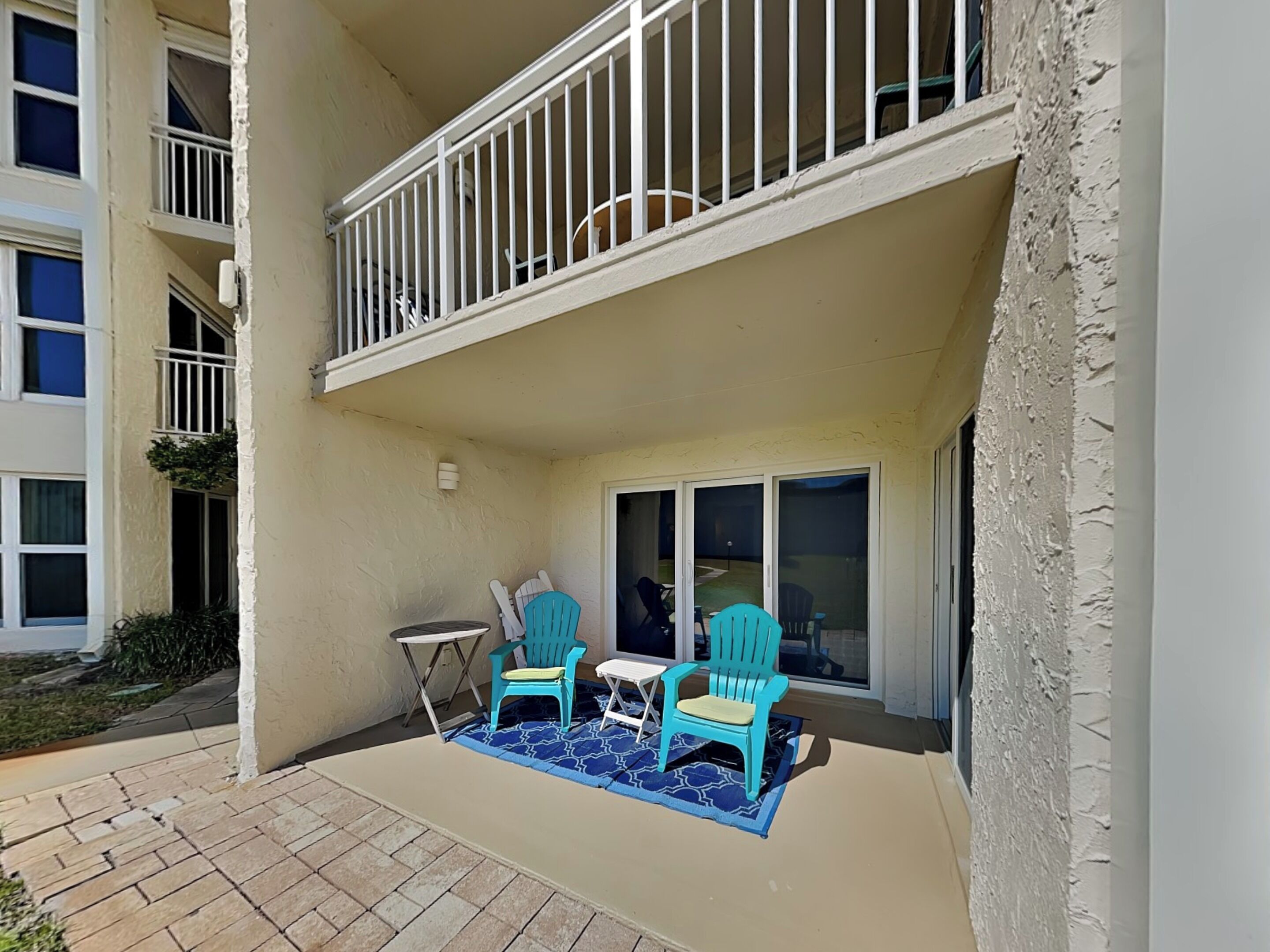 A balcony with two chairs and a small table, a sliding glass door, and a brick pathway.