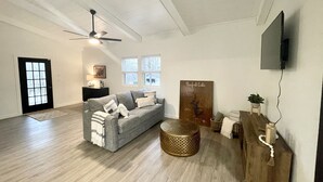A spacious living room with a grey sofa, a coffee table, and a television mounted on the wall.
