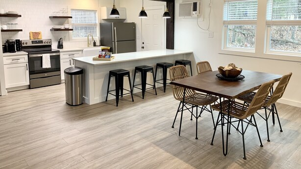 A modern kitchen with a central island, bar stools, and a dining table with wicker chairs.