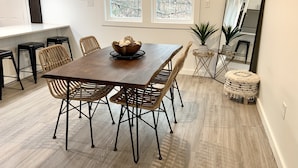A dining area with a wooden table, wicker chairs, and a bowl of fruit.