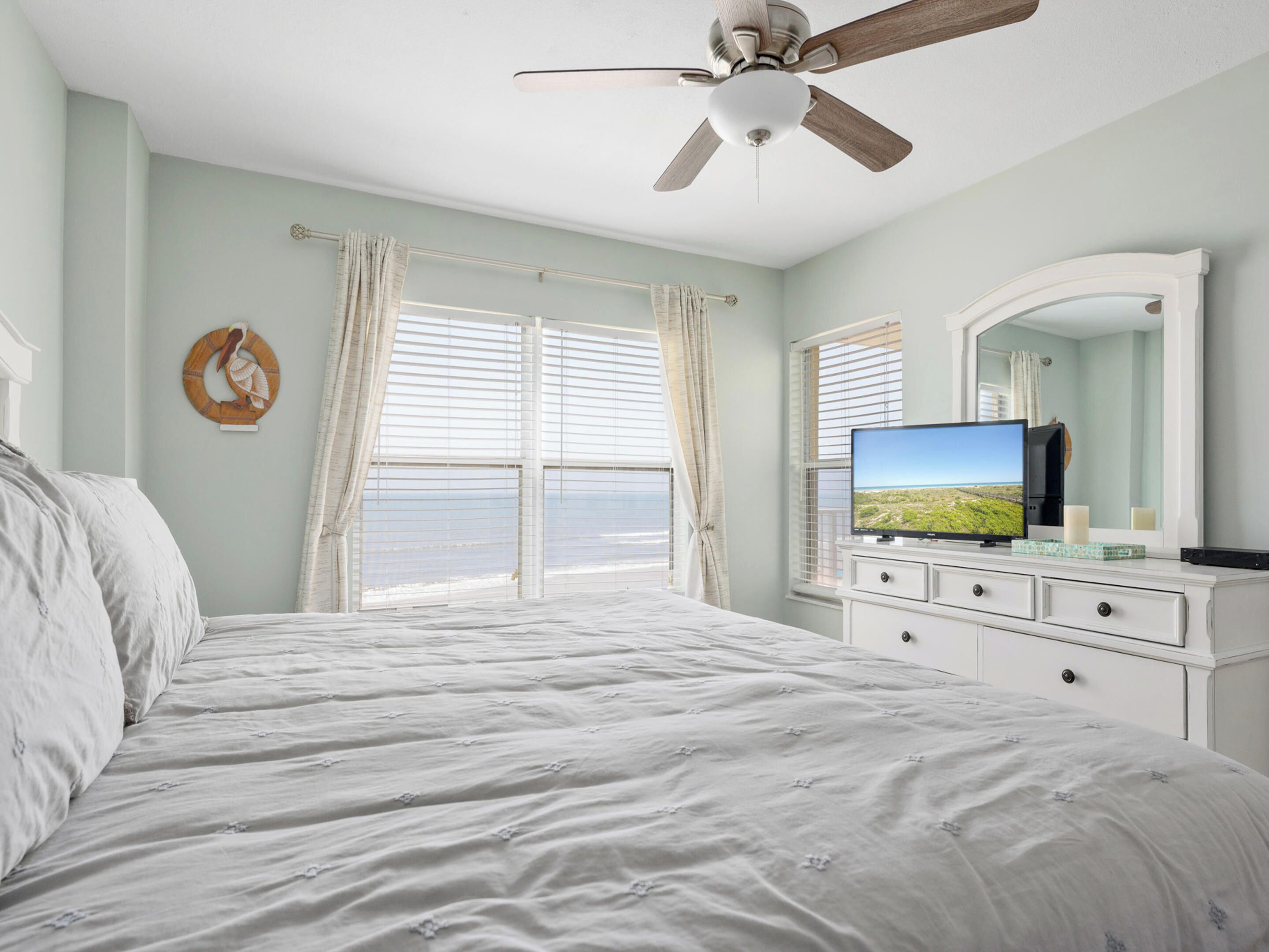 Une chambre à coucher avec un lit, un ventilateur de plafond, une télévision et une fenêtre avec des rideaux.