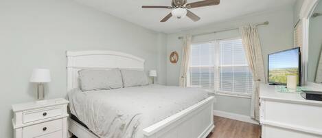 A bedroom with a bed, nightstands, a dresser, a ceiling fan, a window with curtains, and a television.
