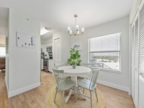 Una cocina moderna con muebles blancos, un comedor con una mesa redonda y sillas, y vistas amplias por grandes ventanales.