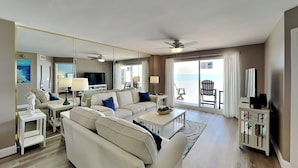 A modern living room with a sofa, coffee table, and TV. There is a balcony with a chair and a table.