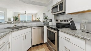 A modern kitchen with white cabinets, stainless steel appliances, granite countertops, and a view to the outside.