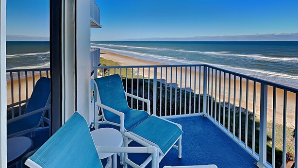 A balcony with a view of the ocean, featuring blue chairs and a table.