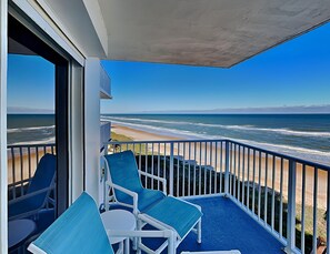 Uma varanda com vista para o oceano, com cadeiras azuis e uma mesa.