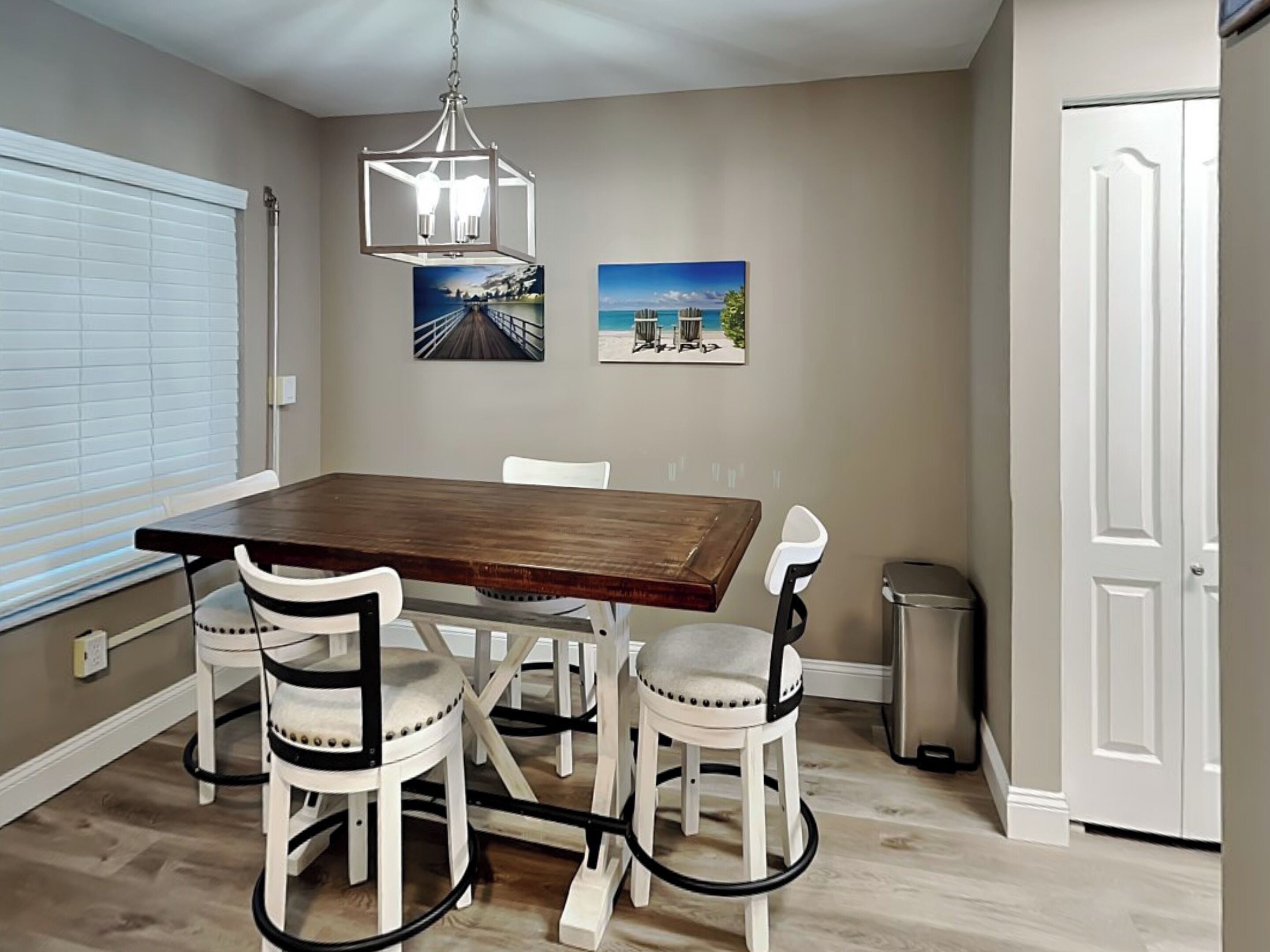 A dining area with a wooden table and four white chairs, a chandelier, and two framed pictures on the wall.