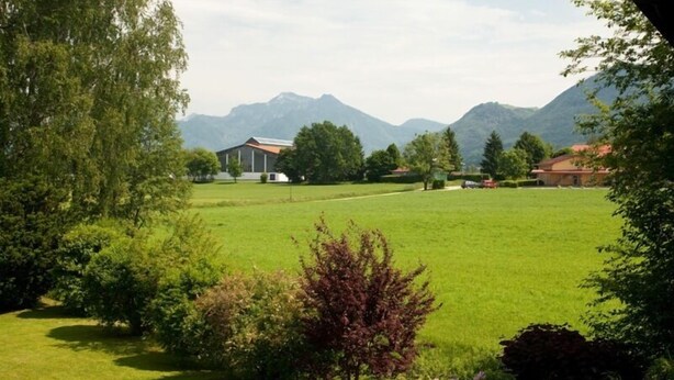Paesaggio rurale con una casa, un campo verde e montagne sullo sfondo.