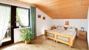 Een slaapkamer met een houten plafond, een bed met bloemenbedrukking, een nachtkastje, een potplant en een raam met gordijnen.