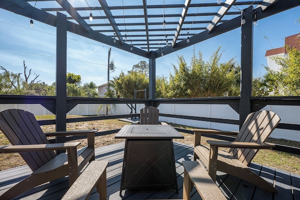 An outdoor patio with a pergola, two Adirondack chairs, and a square table. - Sailing Mood by Distinctive Beach Rentals (Palm Coast)