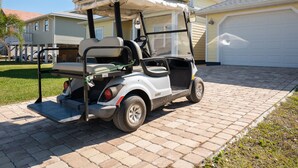 Une voiturette de golf est garée sur une allée pavée devant une maison d’habitation avec un garage.